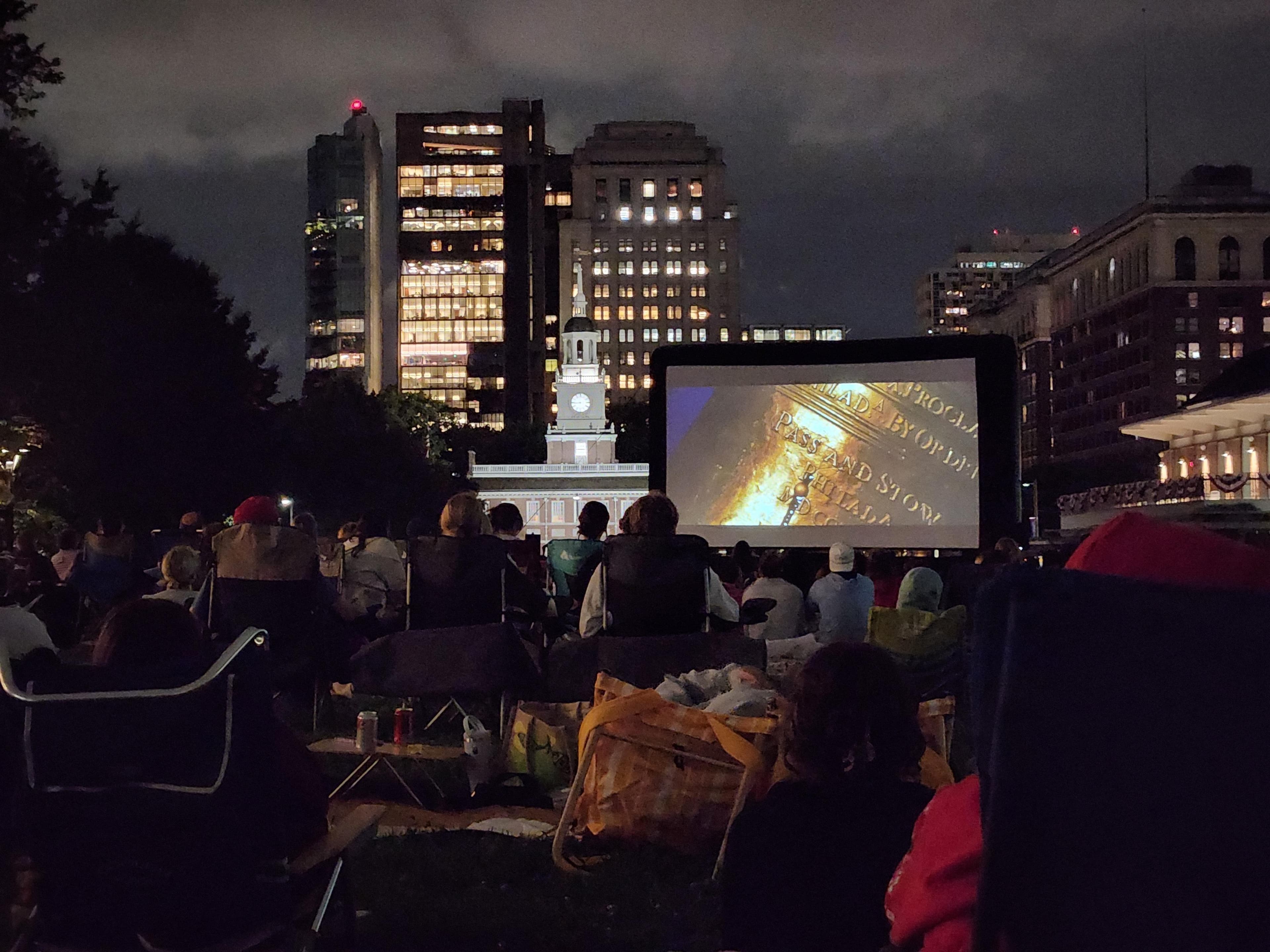A crowd gathered on a grassy mall watching a movie.