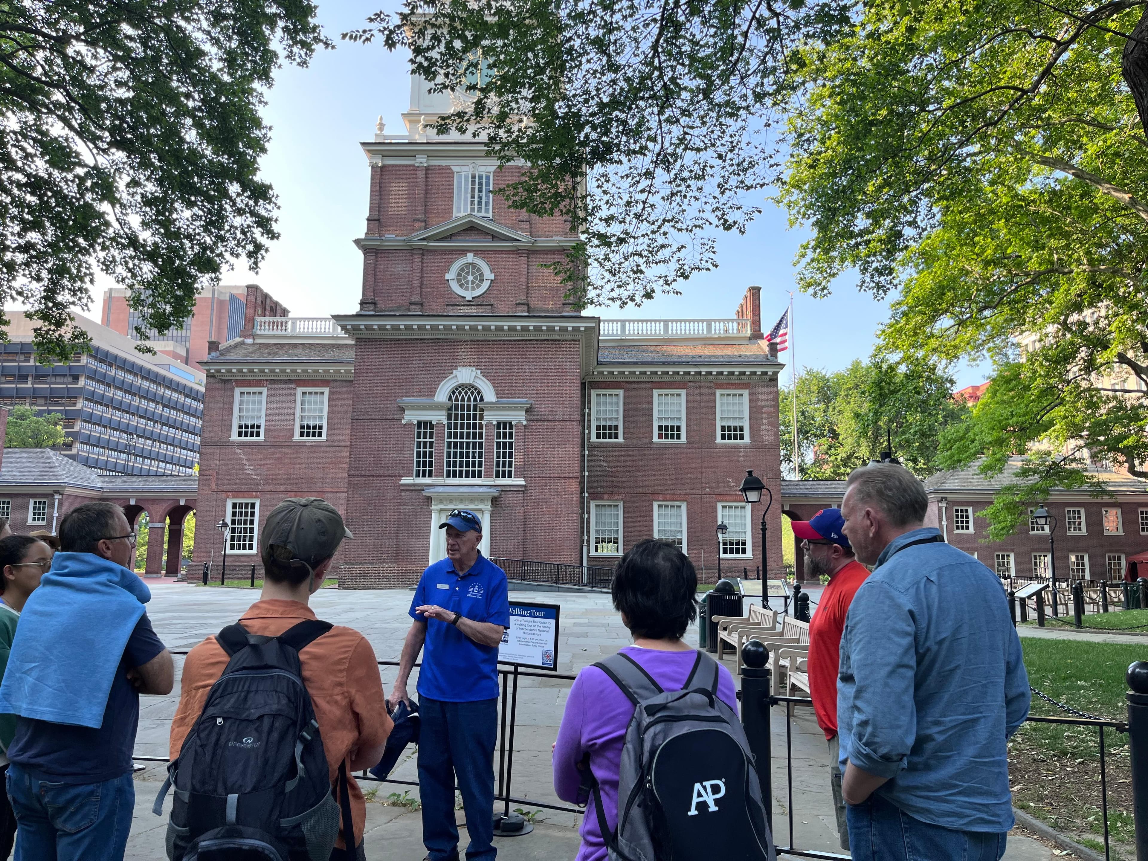 A man in a blue shirt speaks to a crowd of people in front of Independence Hall.