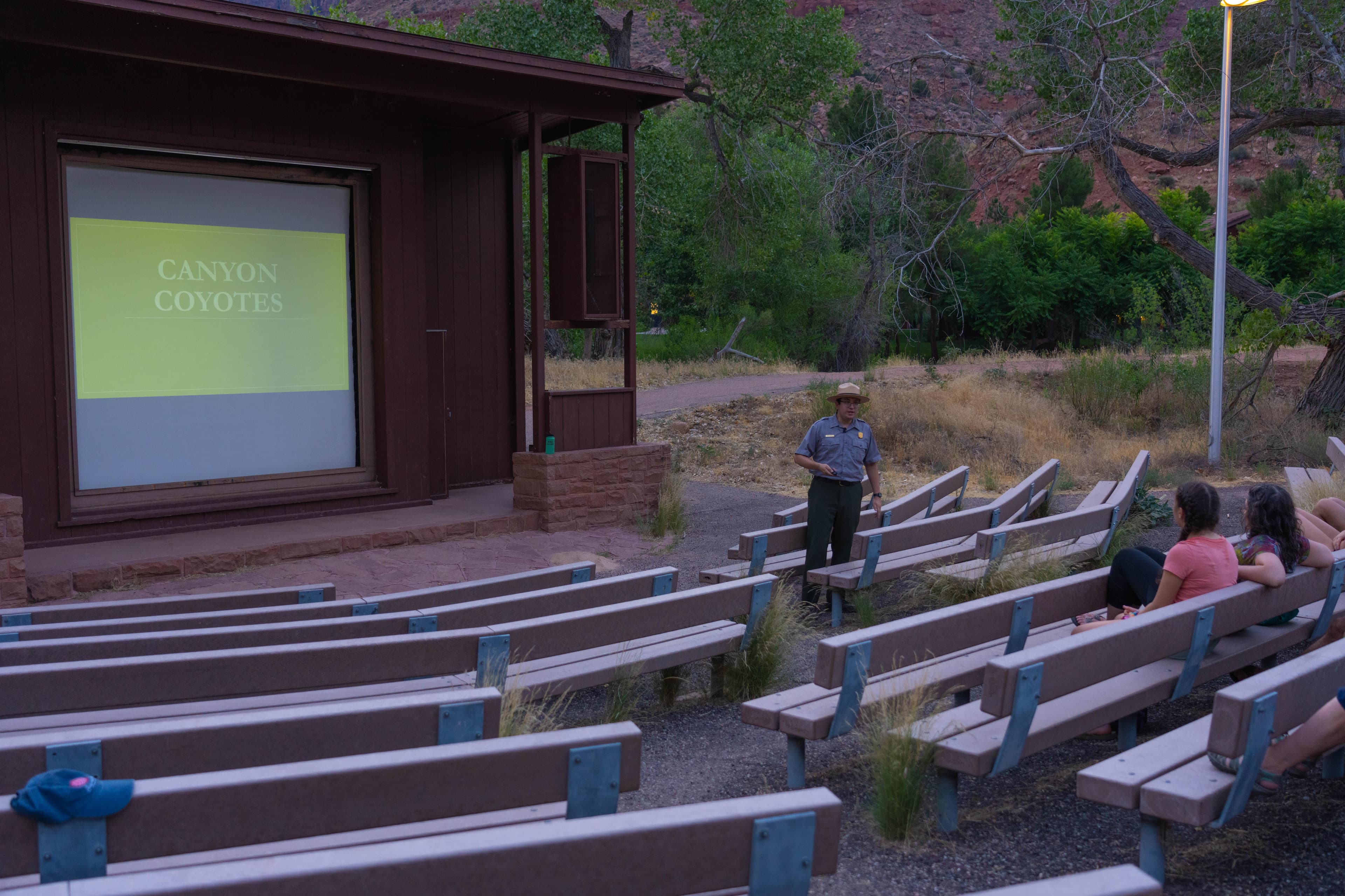 A ranger stands by a white projector screen in an amphitheater of benches.